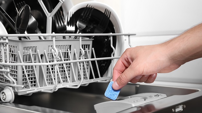 person putting a dishwasher tablet into a dishwasher